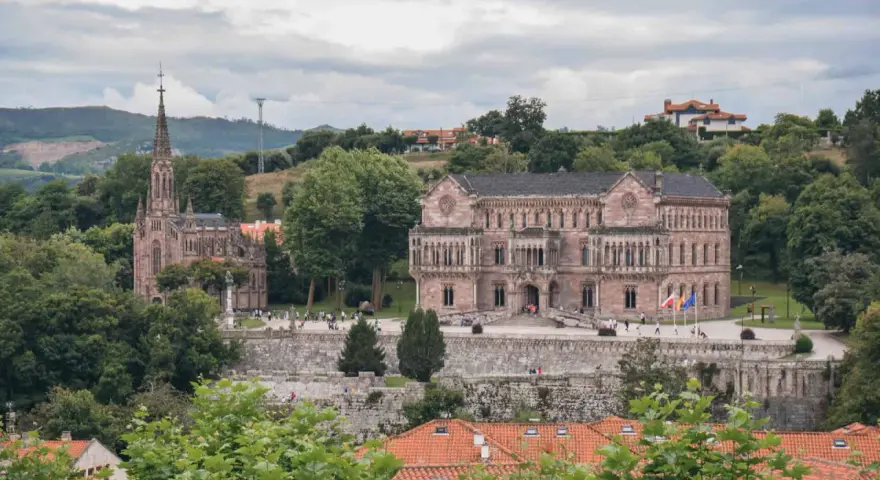 Edificio neogótico y palacio en Comillas, rodeados de vegetación y colinas. Un lugar para ver y disfrutar.