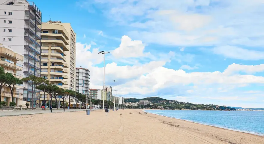 Amplia playa de arena dorada en la playa de Aro centro, con edificios altos a la izquierda y el mar azul a la derecha.