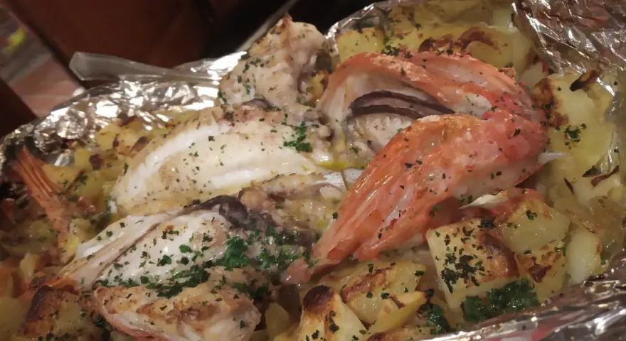 Delicioso pescado y gambas al horno con patatas, un plato típico de la casa Juanita Begur.