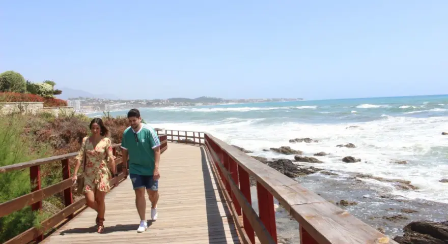 Pareja paseando por un sendero de madera con vistas al mar y la costa de Mijas. ¡Un lugar ideal que ver en Mijas Costa!