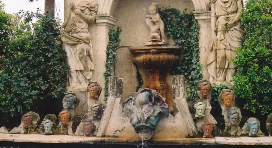 Fuente con estatuas y cabezas de piedra, evocando un antiguo castillo de gala.