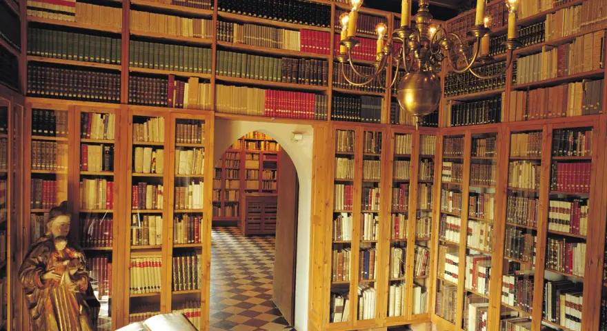 Interior del museu del castell de Peralada, con estanterías repletas de libros antiguos y una lámpara de araña dorada.