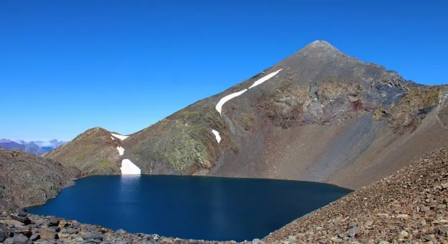 Lago azul profundo en el collado de Tebarray, rodeado de montañas rocosas y con restos de nieve.