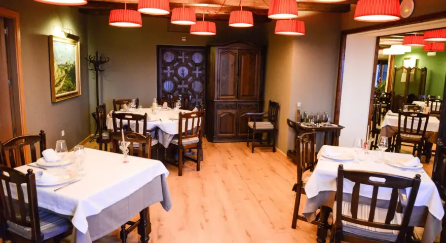 Mesas puestas y listas para comer en Morella. El restaurante tiene lámparas rojas, muebles de madera oscura y un cuadro en la pared.