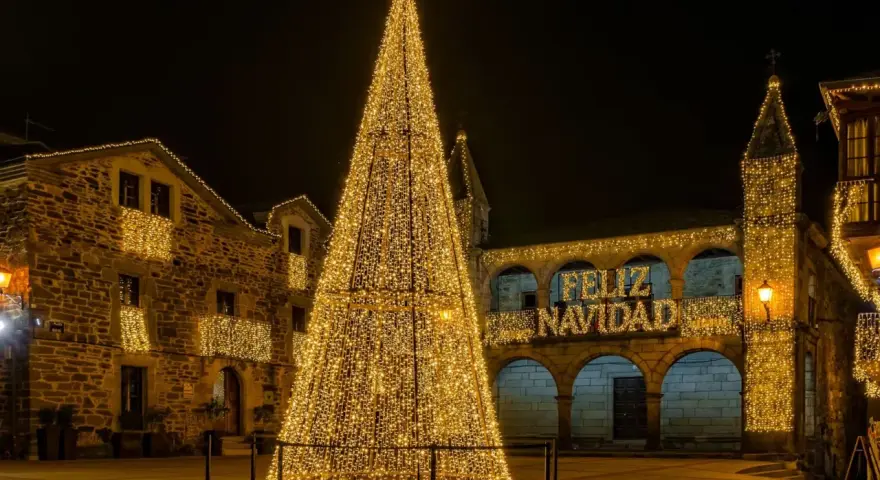 Árbol de Navidad gigante iluminado en una plaza, con edificios adornados y el mensaje "Feliz Navidad". Un lugar ideal que visitar en Navidad en España.
