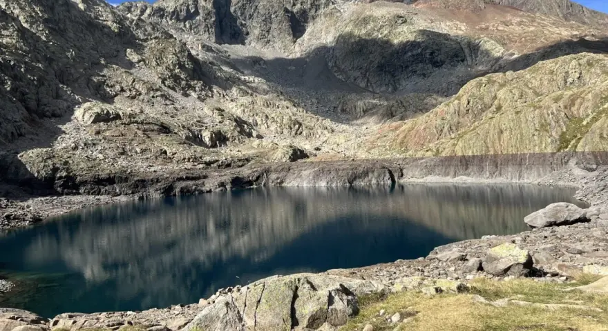 Un lago de montaña de aguas azules profundas, reflejando las cumbres rocosas y el cielo. Un paisaje perfecto para la ruta ibones azules.