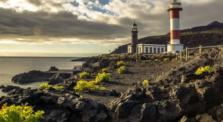 Faros gemelos en la costa rocosa, un destino que ver en La Palma. El mar y el cielo nublado completan la escena.