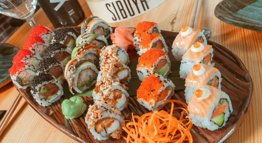 Variedad de sushi en plato marrón, ideal para saber donde comer en Vitoria. Incluye rollos con salmón, huevas de pez volador, aguacate y tempura.
