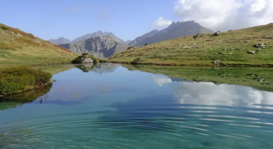 Un sereno ibón de espelunciecha refleja montañas y cielo azul.