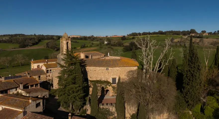 El castell de Gala, con su torre campanario, se alza entre tejados y vegetación, rodeado de verdes colinas bajo un cielo azul.