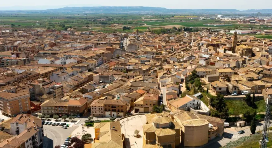 Vista aérea de un pueblo español con tejados de teja, donde se alza la torre de una iglesia. La **ejea de los caballeros** se extiende hasta el horizonte.