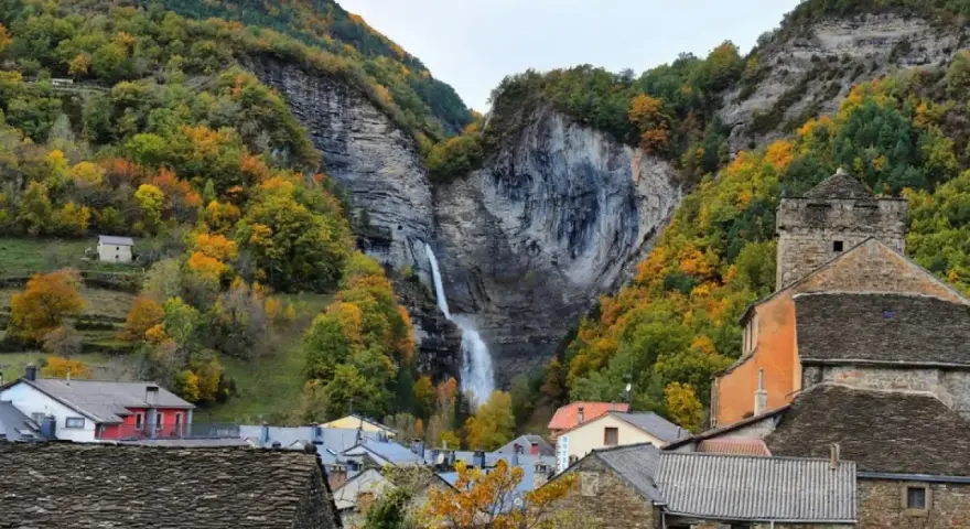 Cascada espectacular en Broto, Huesca, rodeada de bosques otoñales y casas de piedra.