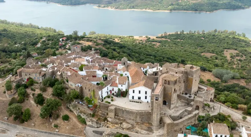 Vista aérea de Castellar de la Frontera, un pueblo blanco con un castillo, rodeado de vegetación y un embalse. Un lugar que evoca la paz de los hippies.