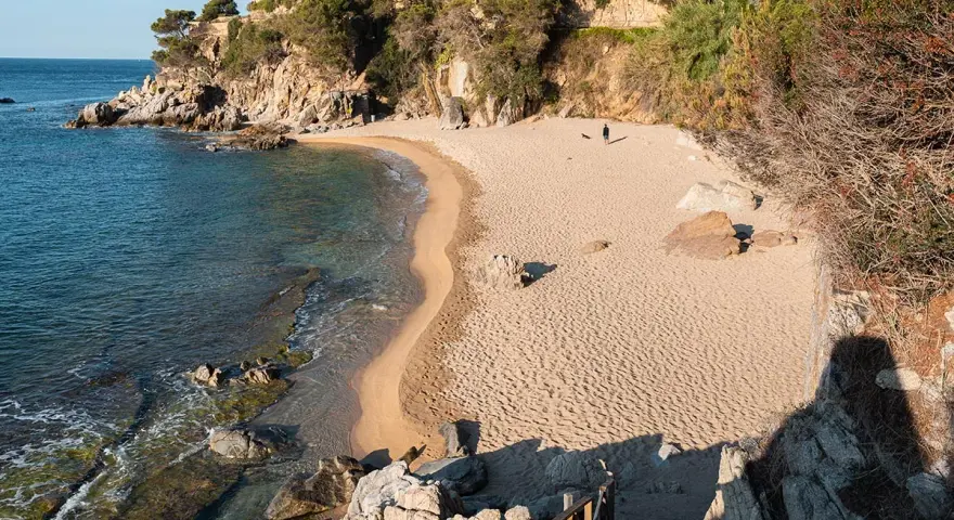 Una persona pasea por la cala belladona, con arena dorada y aguas cristalinas.