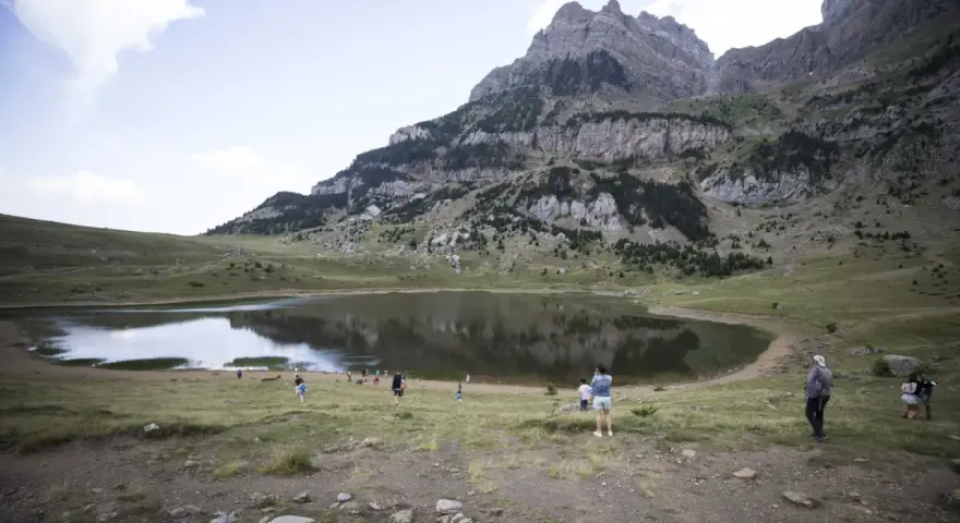 Gente paseando cerca de un lago en el valle de Tena, ideal para rutas de senderismo. Montañas escarpadas al fondo.