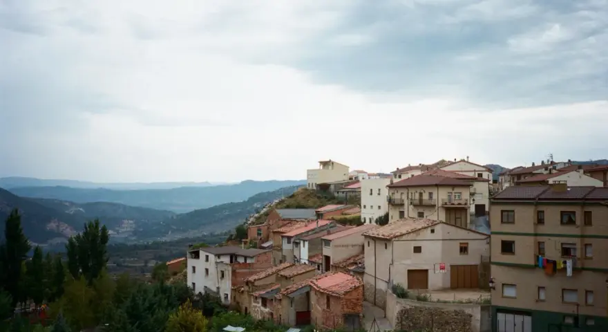 Pueblo español en ladera, con casas de tejados rojos y vistas a montañas. Se ven más de las matas verdes que rodean el asentamiento.