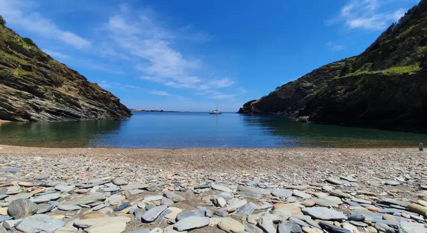 Cala Sa Sabolla, una bahía rocosa con aguas cristalinas y un velero solitario.