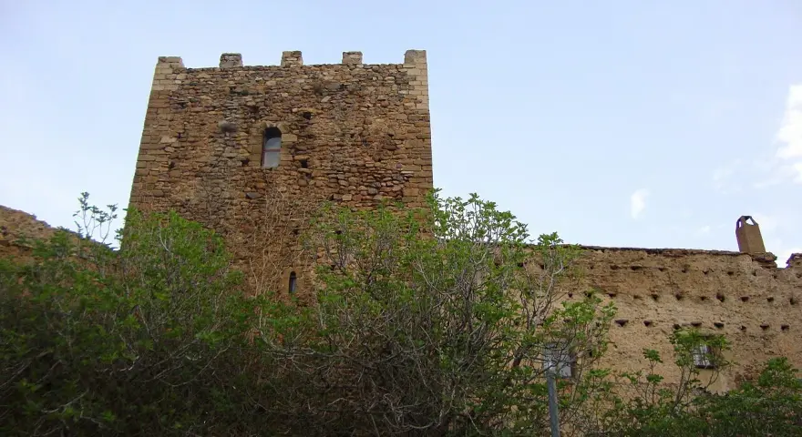 Castillo de piedra con almenas y vegetación frondosa delante.