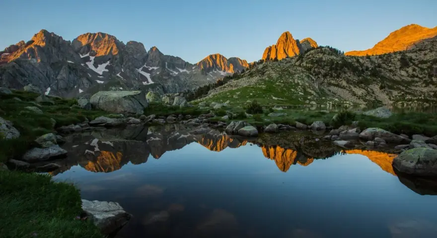 Reflejo dorado de montañas en un lago sereno del **parque natural Posets Maladeta** al amanecer.