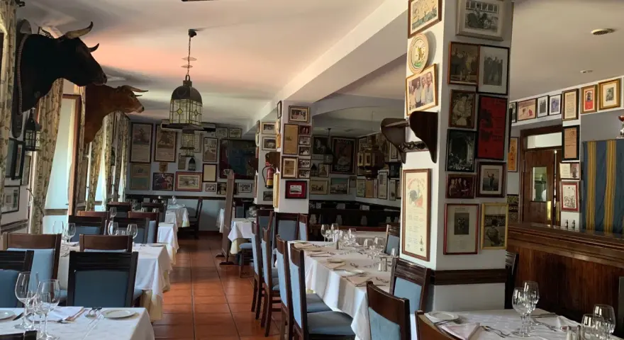 Mesas puestas para comer en ronda, decorado con cabezas de toro y carteles taurinos.