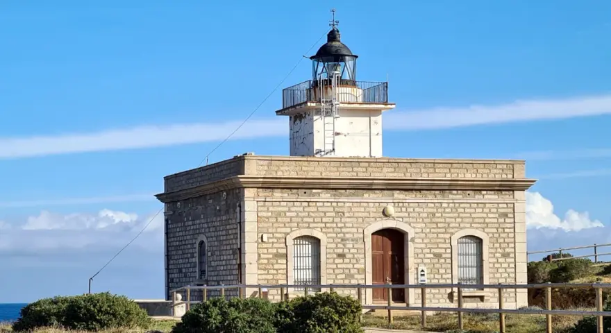 Faro de piedra con torre blanca y cúpula negra, vigilando el mar azul cerca del far port de la selva.
