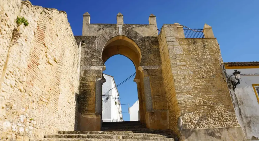 Antigua puerta de Medina Sidonia, con escalinata de piedra y cielo azul. Merece la pena visitar Medina Sidonia.