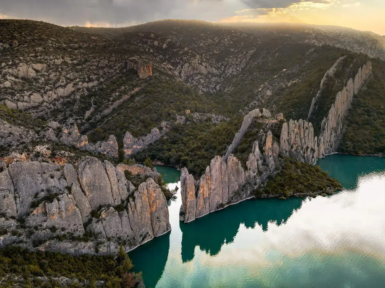 Impresionantes formaciones rocosas y un lago turquesa en Finestres, Huesca, bajo un cielo dramático.