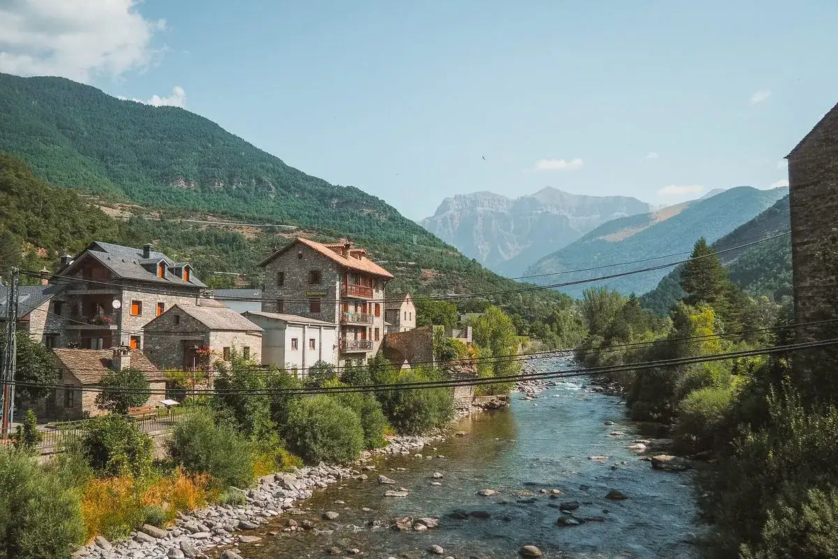 Pueblo de monta&ntilde;a con casas de piedra junto a un r&iacute;o. El broto huesca se alza majestuoso entre verdes monta&ntilde;as.