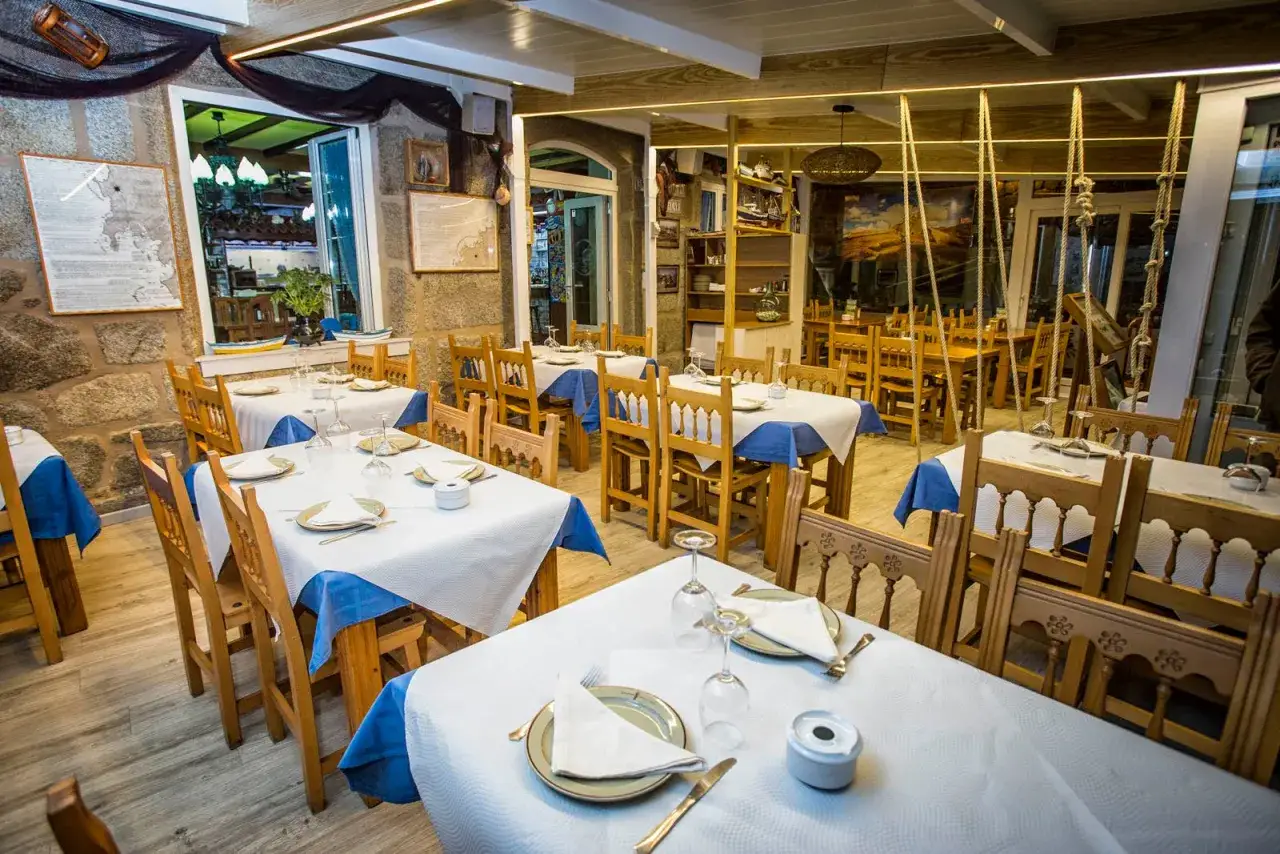 Mesas puestas en un restaurante marinero, ideal para comer en Mux&iacute;a. Decoraci&oacute;n r&uacute;stica con redes y mapas.