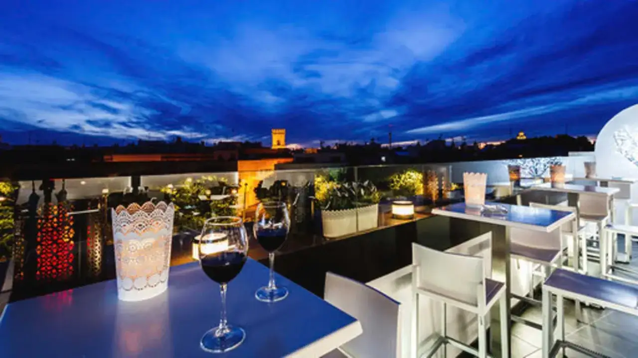 Dos copas de vino tinto en una terraza con vistas a los bares de Sevilla al anochecer.