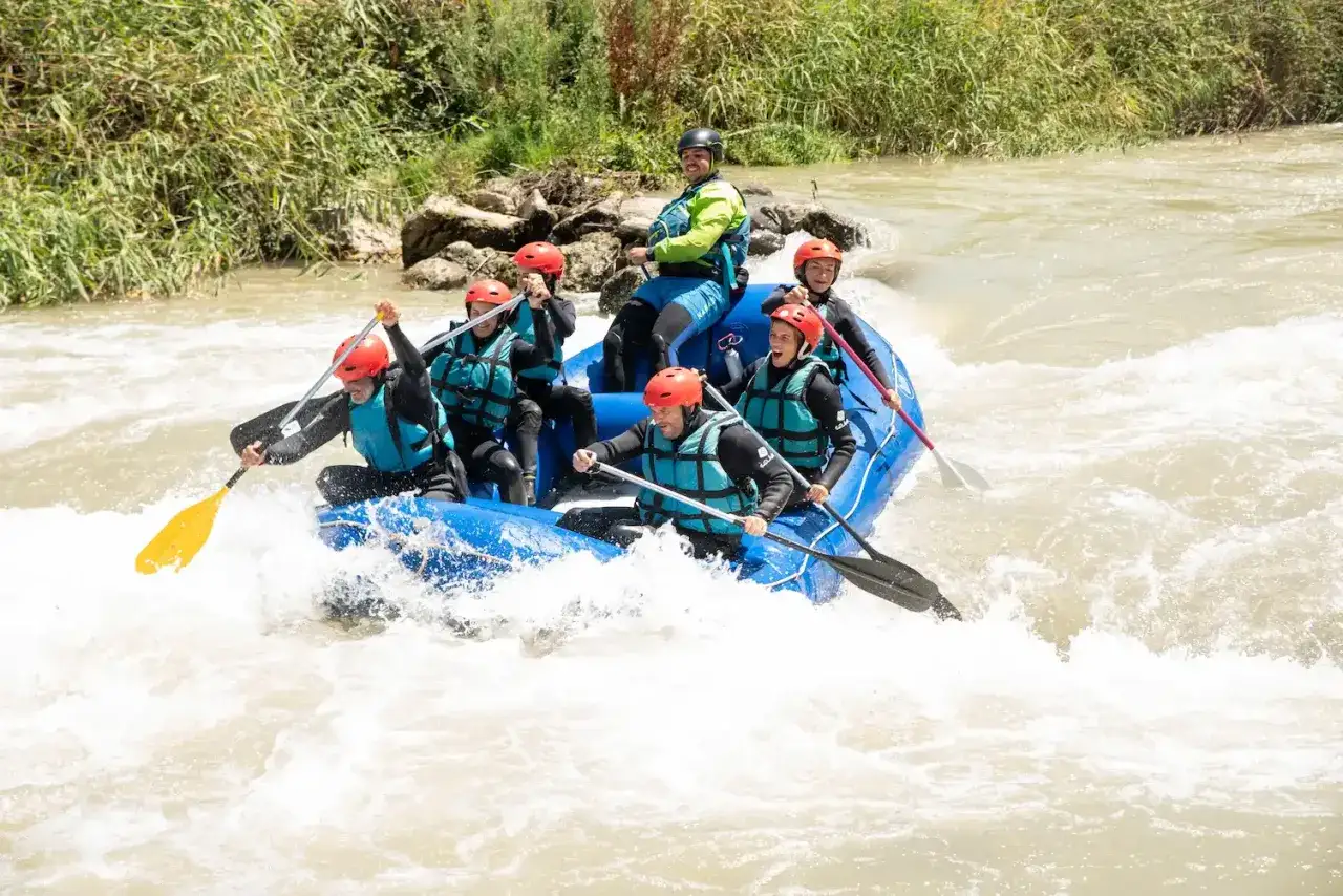 Grupo en balsa azul navegando rápidos turbulentos, una aventura de que es rafting.