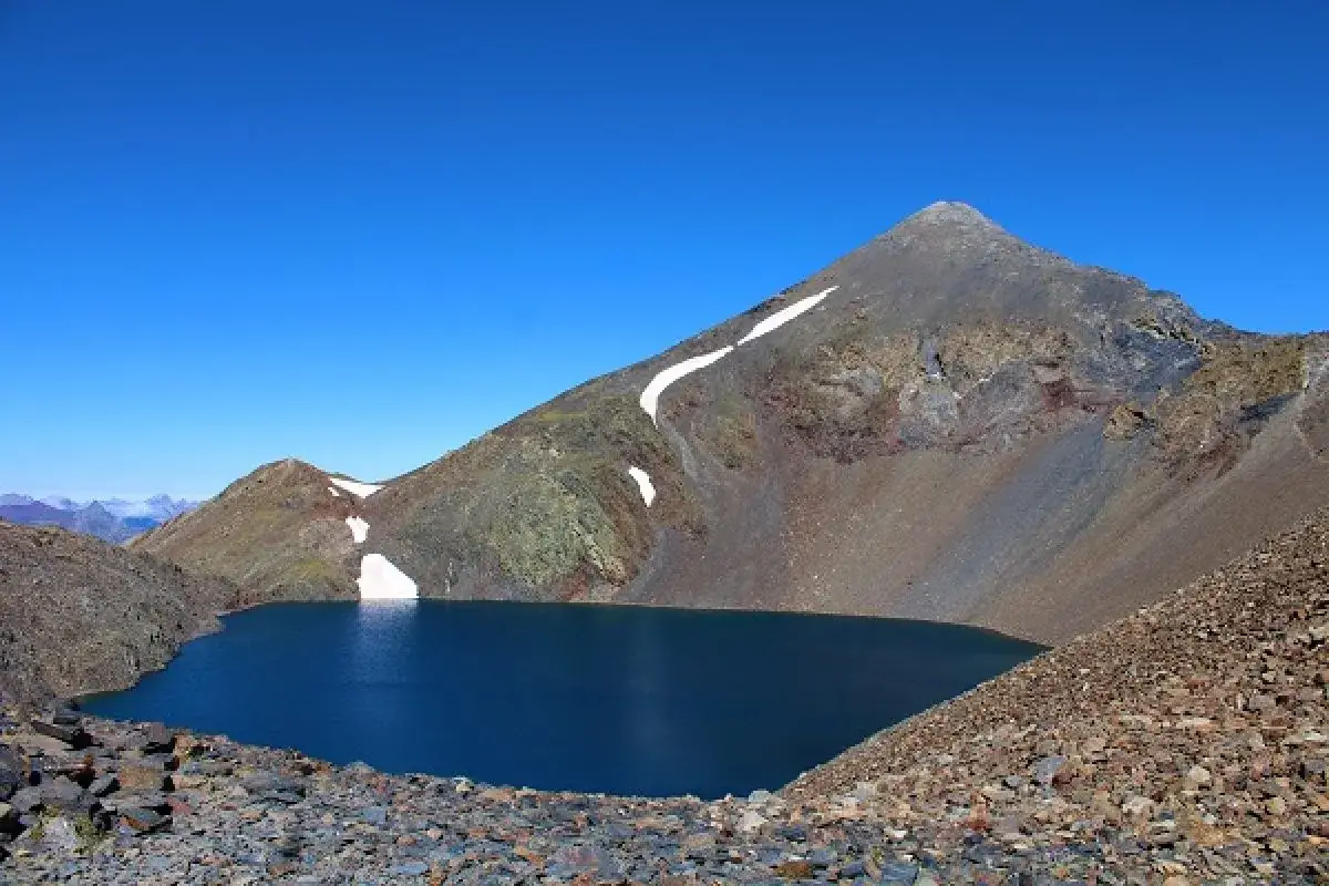 Lago azul profundo en el collado de Tebarray, rodeado de montañas rocosas y con restos de nieve.