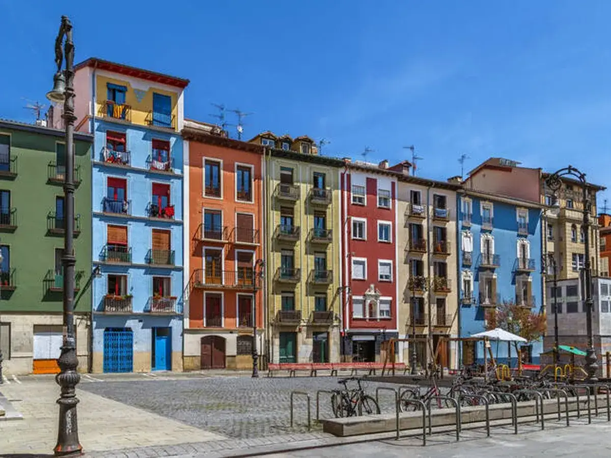 Fachada de edificios coloridos en una plaza, ideal para saber qu&eacute; ver en Pamplona. Hay bicicletas aparcadas y un parque infantil.