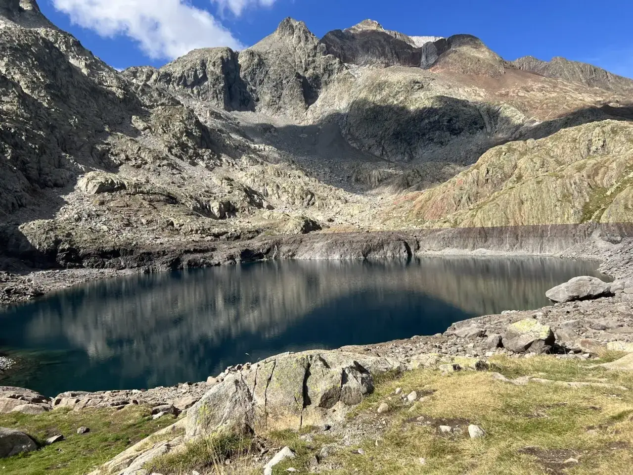 Un lago de montaña de aguas azules profundas, reflejando las cumbres rocosas y el cielo. Un paisaje perfecto para la ruta ibones azules.