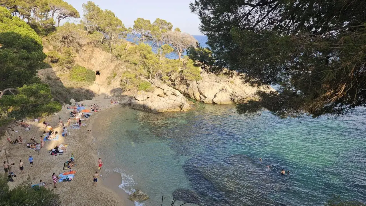 Gente disfruta del sol y el mar en la cala belladona, con aguas cristalinas y rocas escarpadas.
