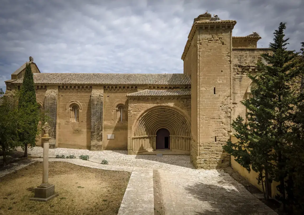 Monasterio de Villanueva de Sigena, con su imponente portada románica y cigüeñas en el campanario.