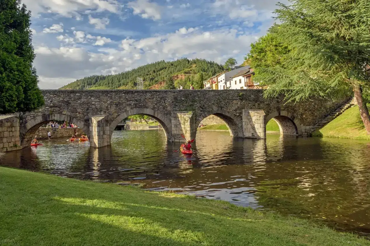 Un puente de piedra con arcos sobre un río donde navegan kayaks. Gente pasea por el puente y la orilla. ¡Un día perfecto para ver Molina seca!