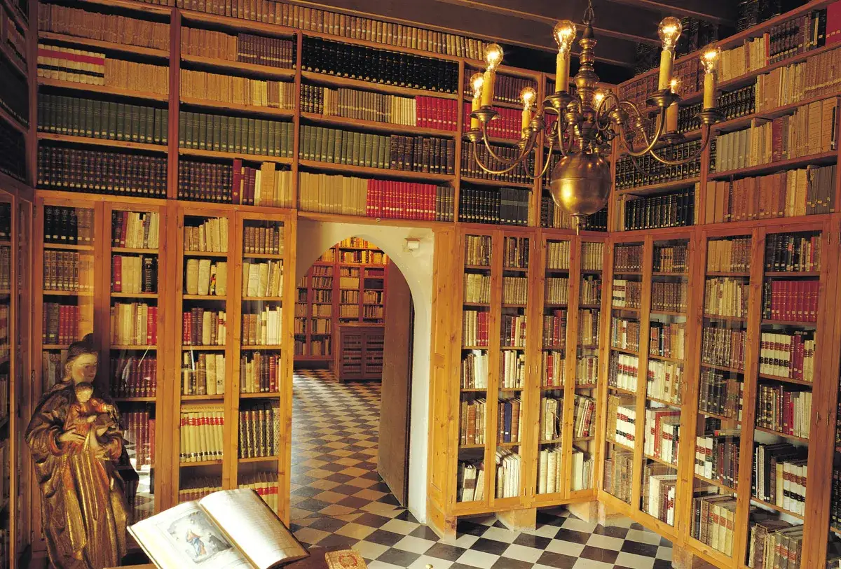 Interior del museu del castell de Peralada, con estanter&iacute;as repletas de libros antiguos y una l&aacute;mpara de ara&ntilde;a dorada.