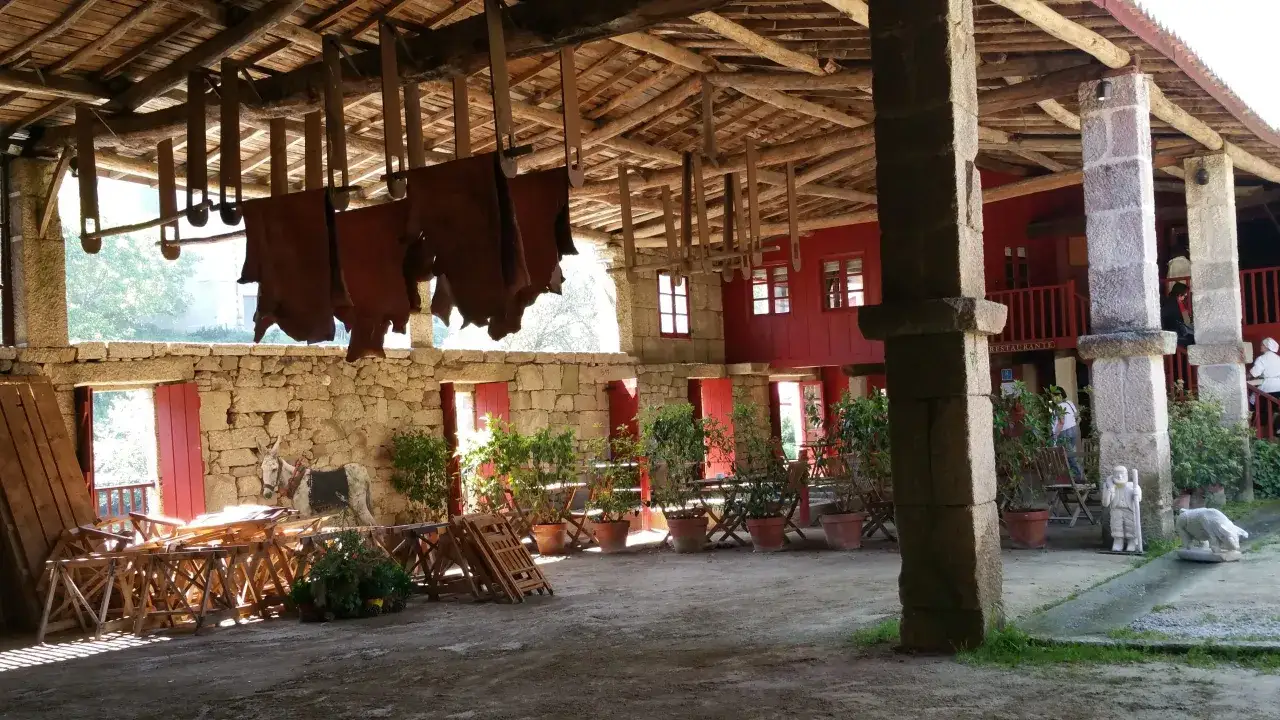 Un lugar rústico con cueros colgados, perfecto para comer en Allariz. Mesas, sillas y un burro decoran el patio.