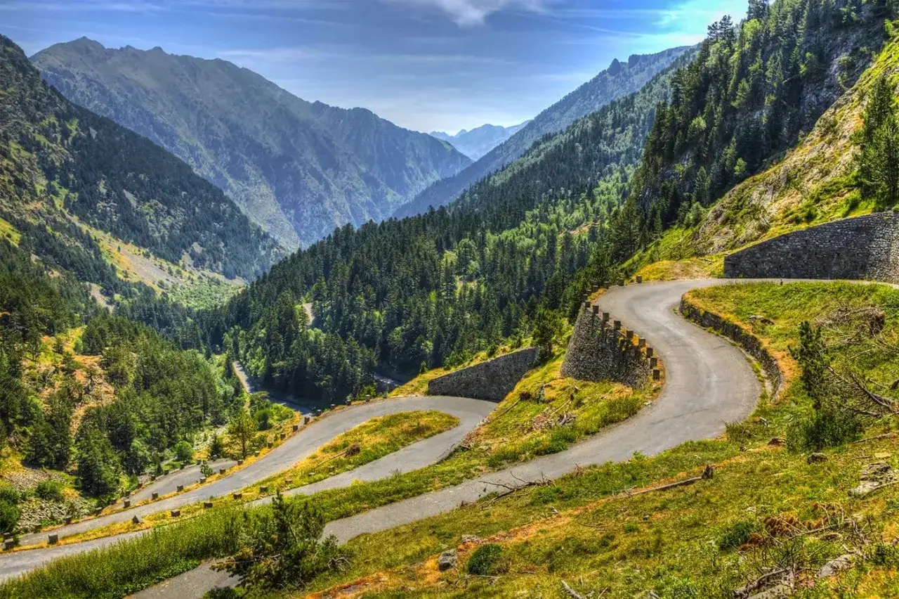 Serpenteante carretera en las rutas pirineos, rodeada de bosques frondosos y montañas imponentes bajo un cielo azul.
