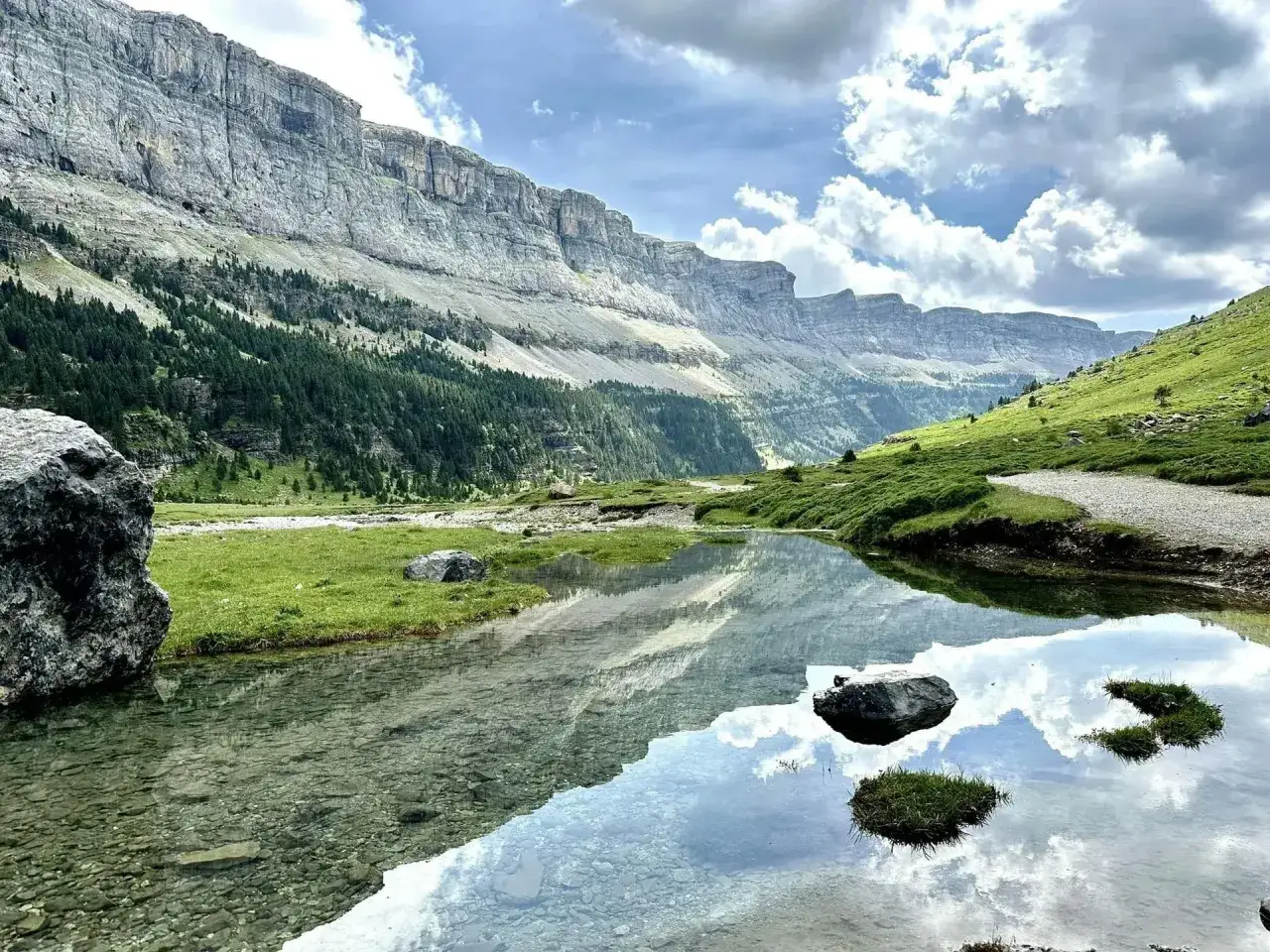 Espectacular montaña de Pirineos con un lago cristalino reflejando el cielo y las imponentes paredes rocosas.