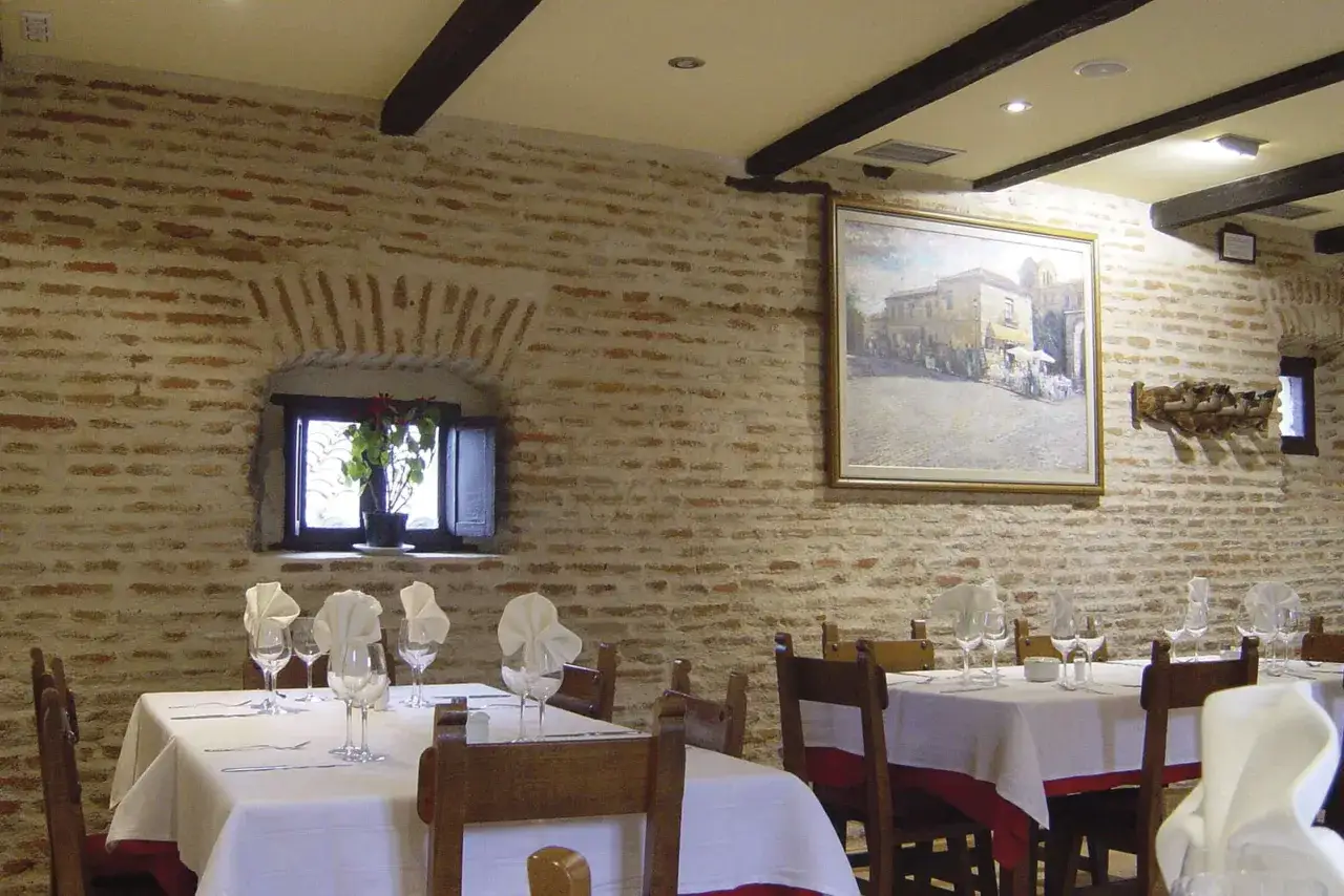 Mesas puestas en un restaurante con paredes de ladrillo visto. Ideal para saber donde comer en Ávila y disfrutar de una cena acogedora.