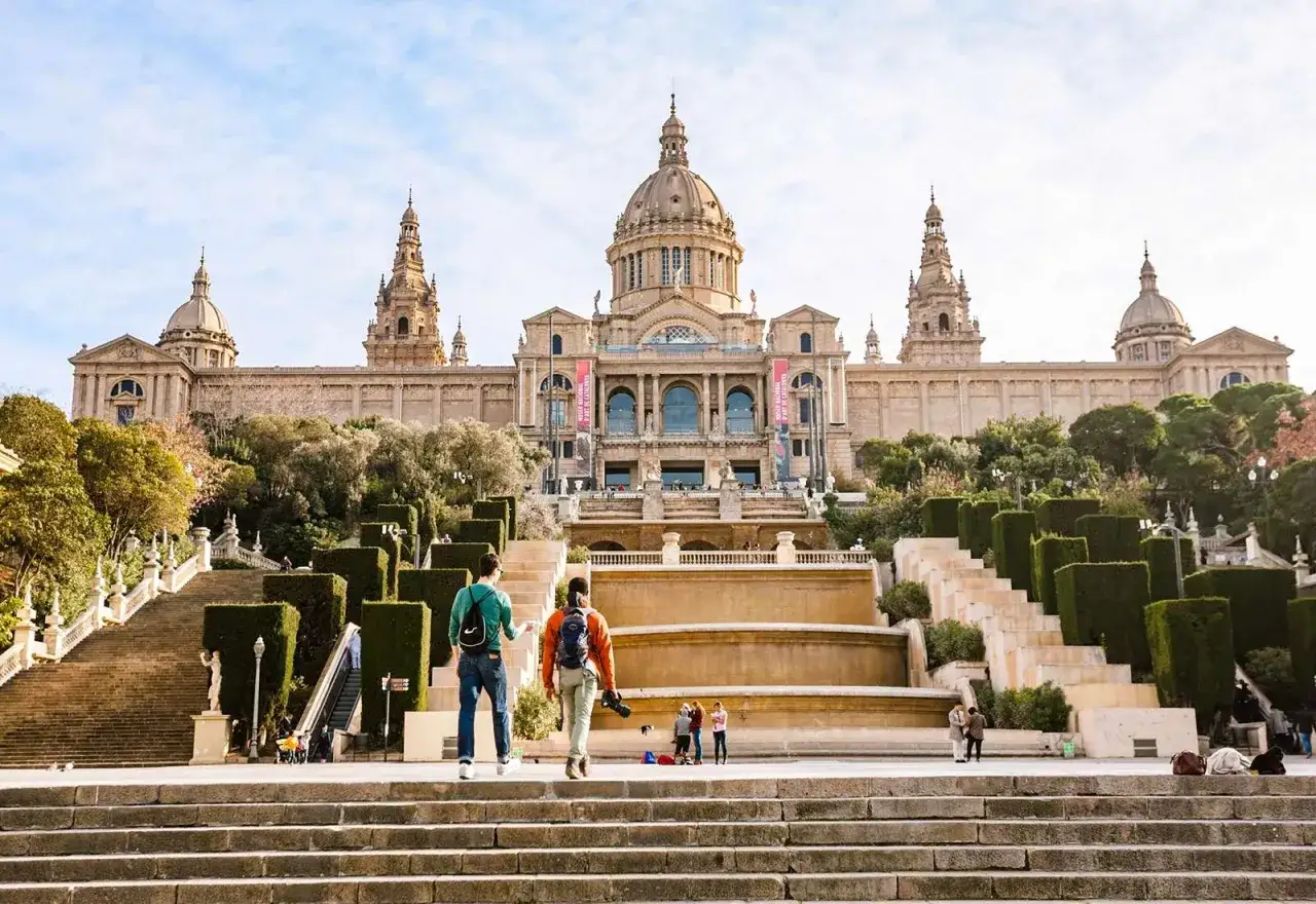 Dos personas suben escaleras hacia el majestuoso Palacio Nacional, uno de los museos de Barcelona, con su imponente cúpula y jardines.