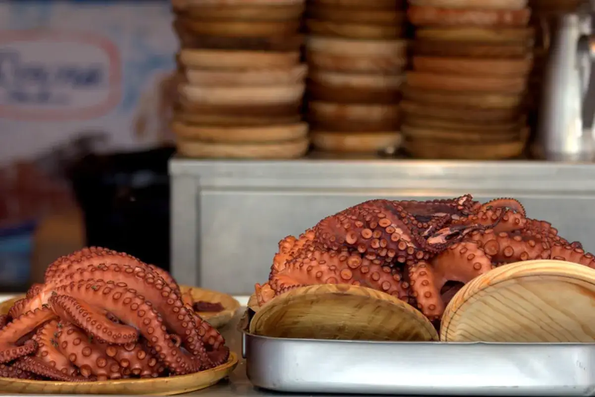 Pulpos cocidos listos para comer en Pontedeume, con pilas de platos de madera al fondo.