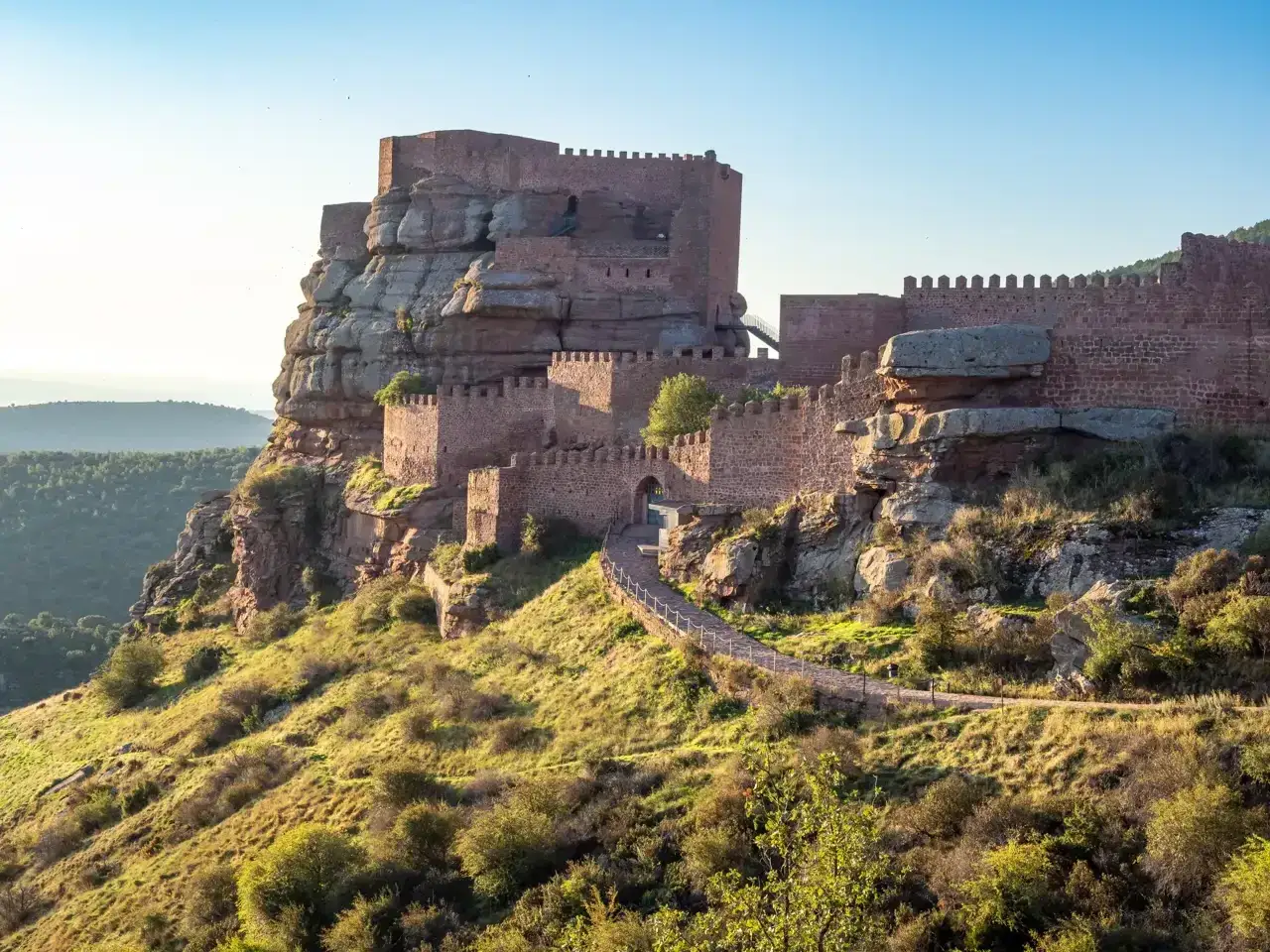 El imponente castillo de Peracense se alza sobre un peñón rocoso, con murallas de piedra rojiza y un camino serpenteante que invita a explorarlo.