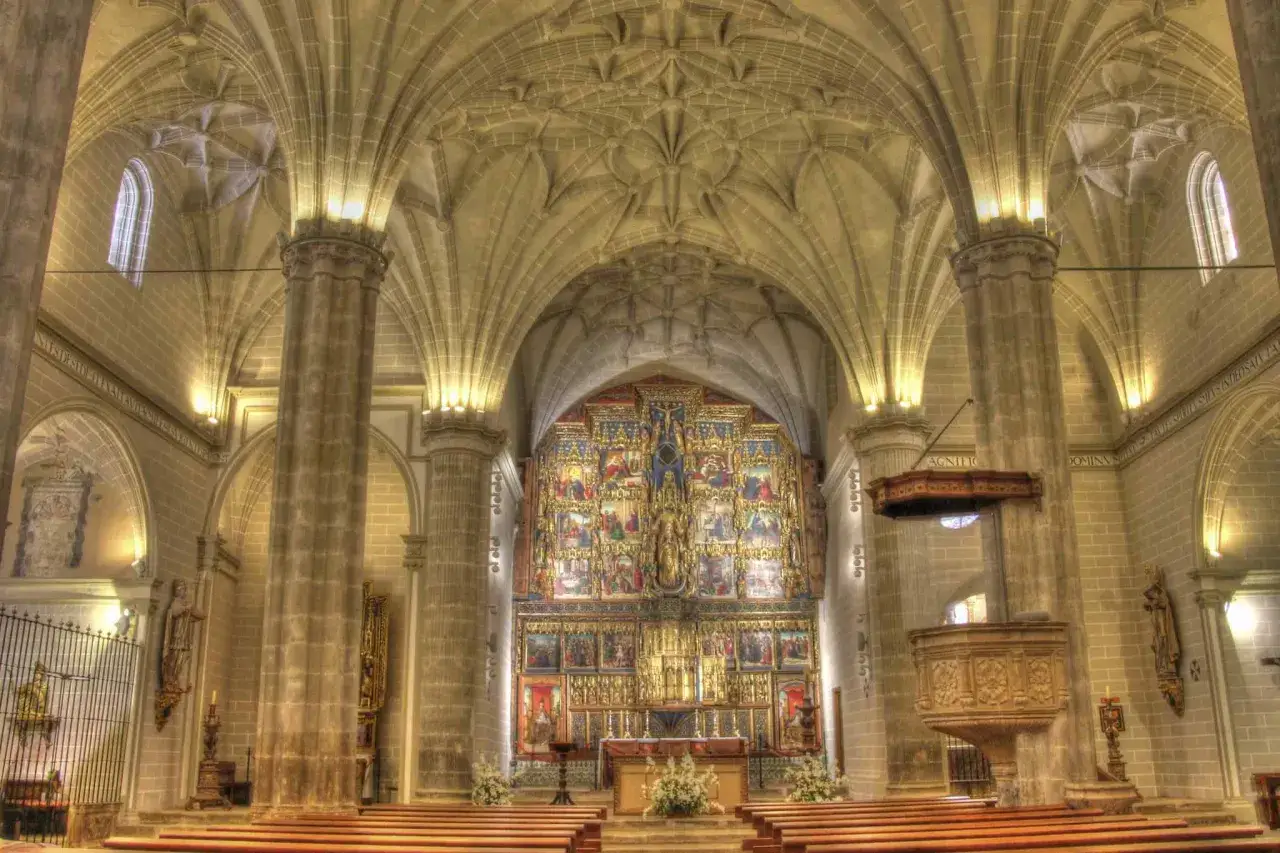 Interior de la colegiata de Bólea, con un retablo dorado y bóvedas de crucería.