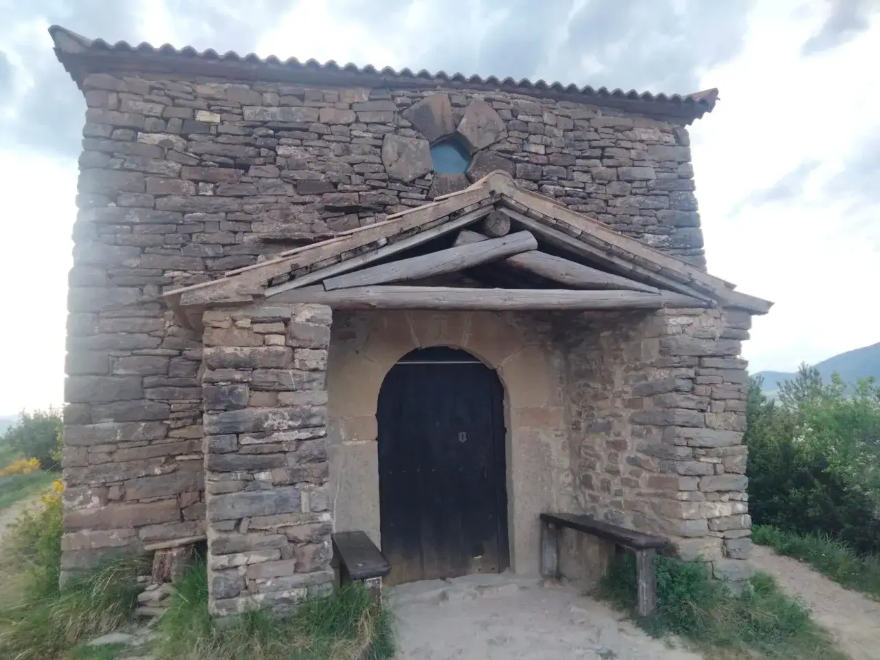 Las ermitas de Tella, construidas en piedra, invitan a la contemplaci&oacute;n. Una puerta oscura y un banco de madera esperan bajo un tejado r&uacute;stico.