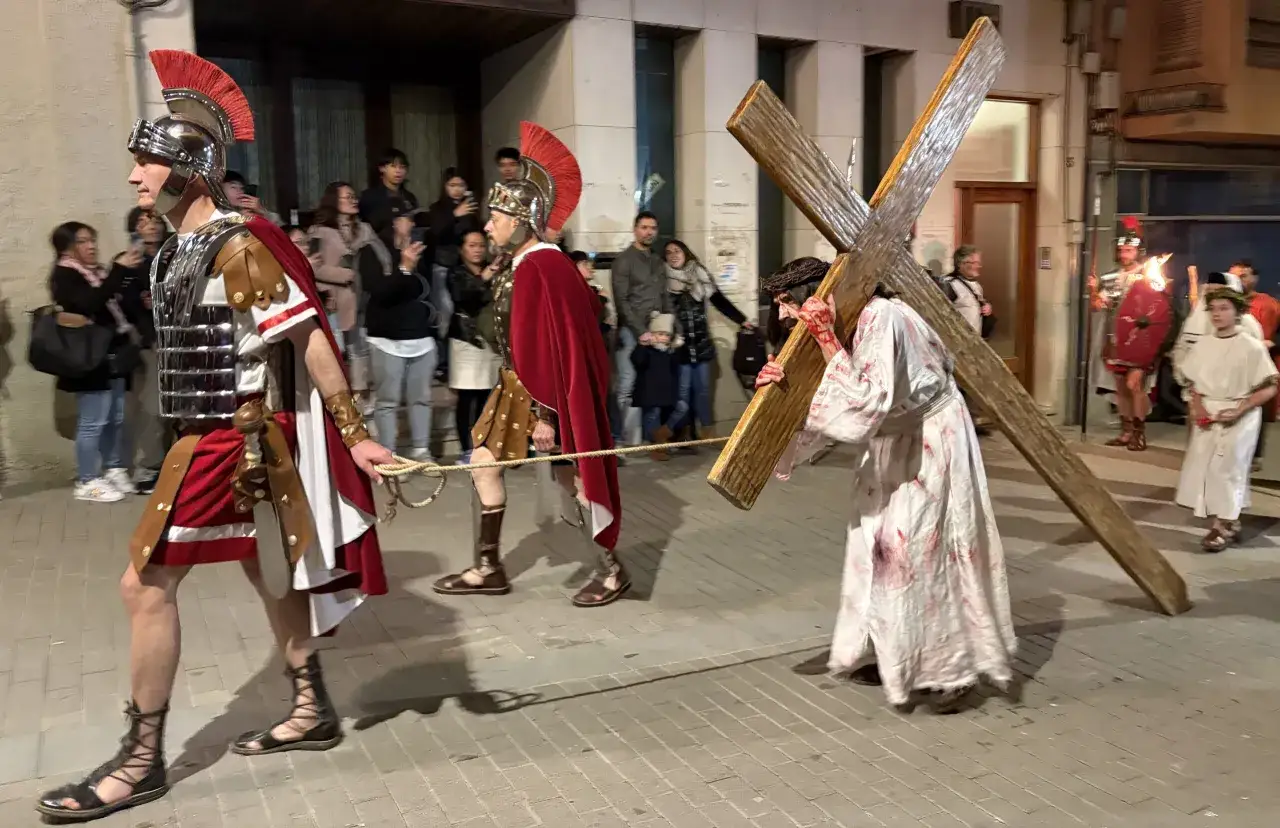 Representación del vía crucis en Sant Hilari. Jesús, con túnica ensangrentada, carga la cruz, guiado por soldados romanos.