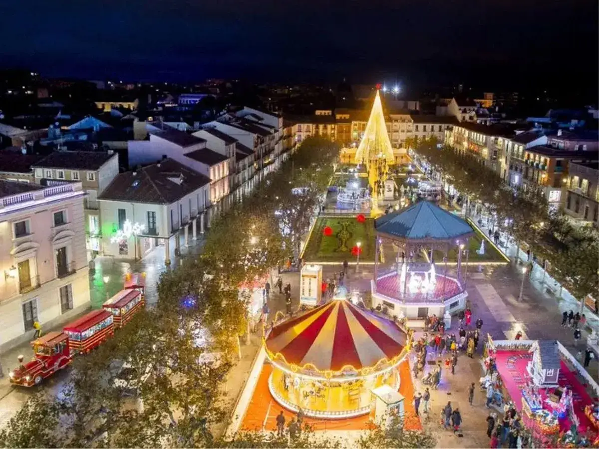 Un carrusel y un tren iluminados en una plaza festiva, ideal para saber qué visitar en Navidad en España.
