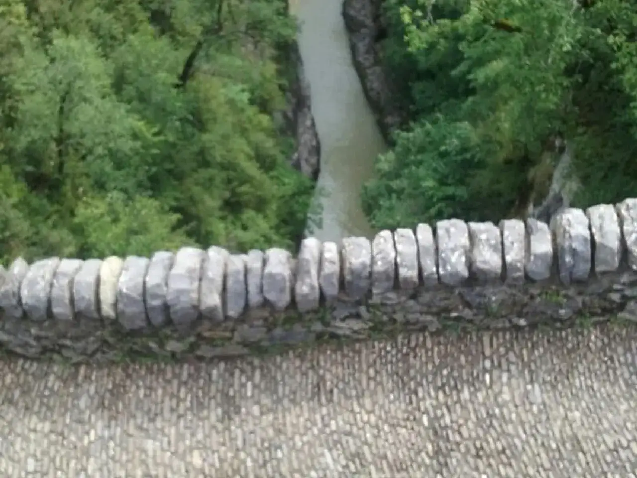 Muro de piedra sobre el cañón de Añisclo, con un río serpenteando entre árboles frondosos.